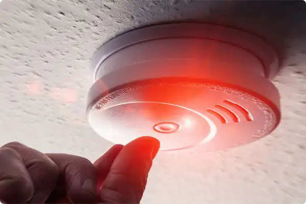 Finger pressing the test button on a ceiling smoke detector