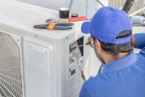 A professional HVAC specialist in St. Louis, MOwearing a blue uniform while repairing a commercial air conditioning unit that had a part loose and created banging sounds.