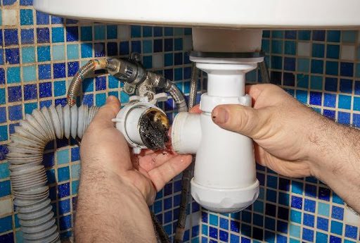 A plumber detaching a white plumbing pipe from a bathroom sink that is clogged and requires professional drain cleaning services in Affton, MO. For drain cleaning services, contact your local plumber.