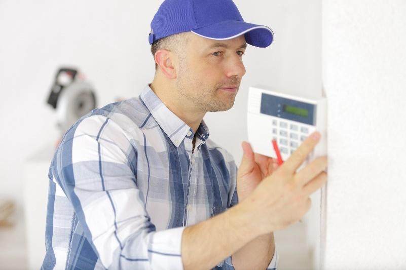 An HVAC technician in a blue plaid shirt and a blue hat providing thermostat repair services to a residential home in St. Louis, MO.