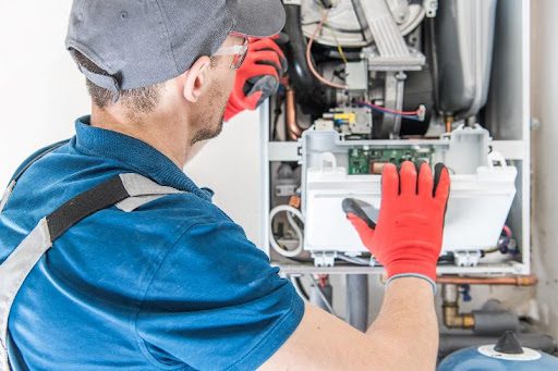 A furnace repair technician wearing red gloves and inspecting a residential heating system that needs furnace repair services in Overland, MO.